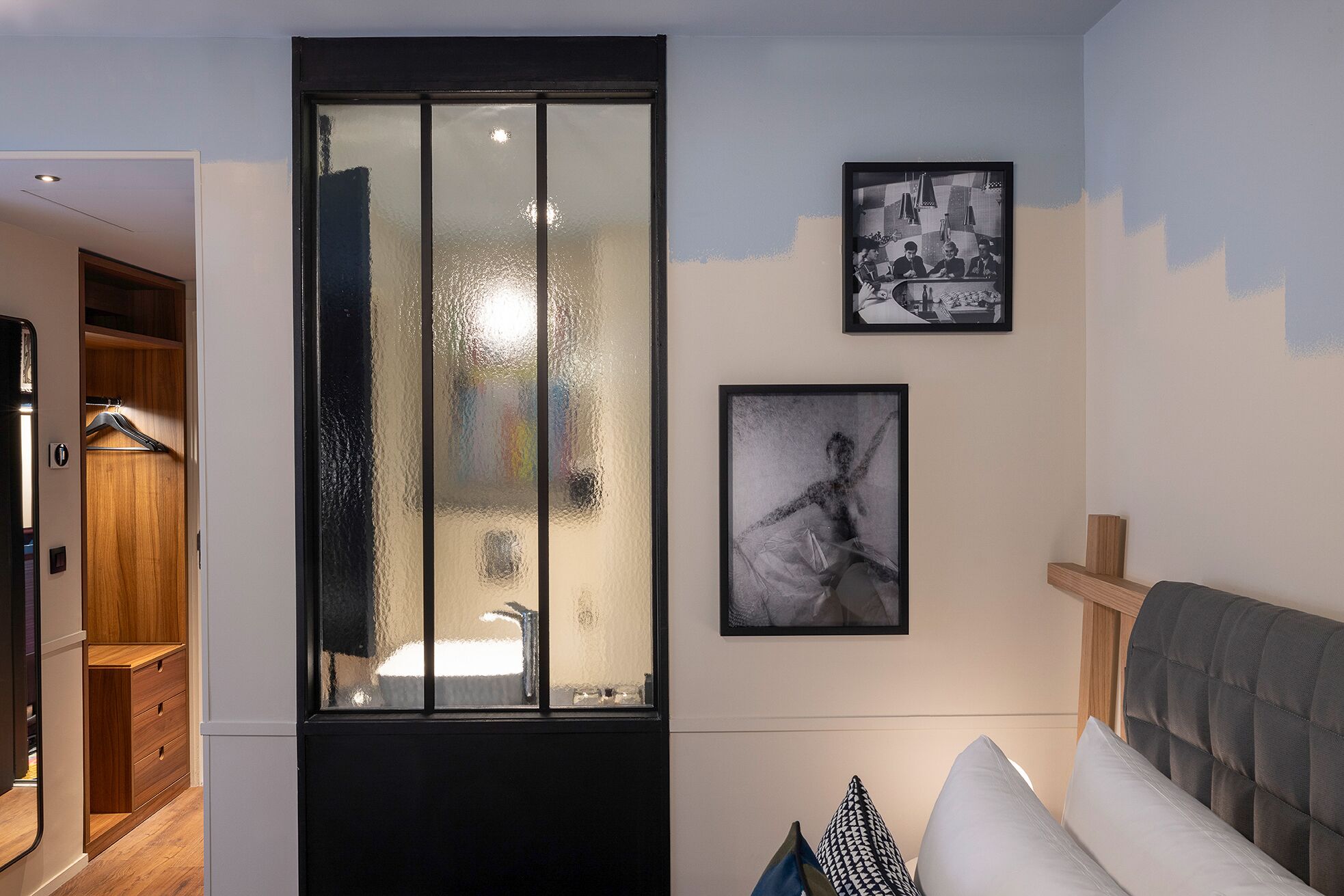 Un salon moderne doté d’une porte-fenêtre coulissante donnant sur une salle de bain, d’un canapé avec des coussins et de deux photographies encadrées accrochées au mur.