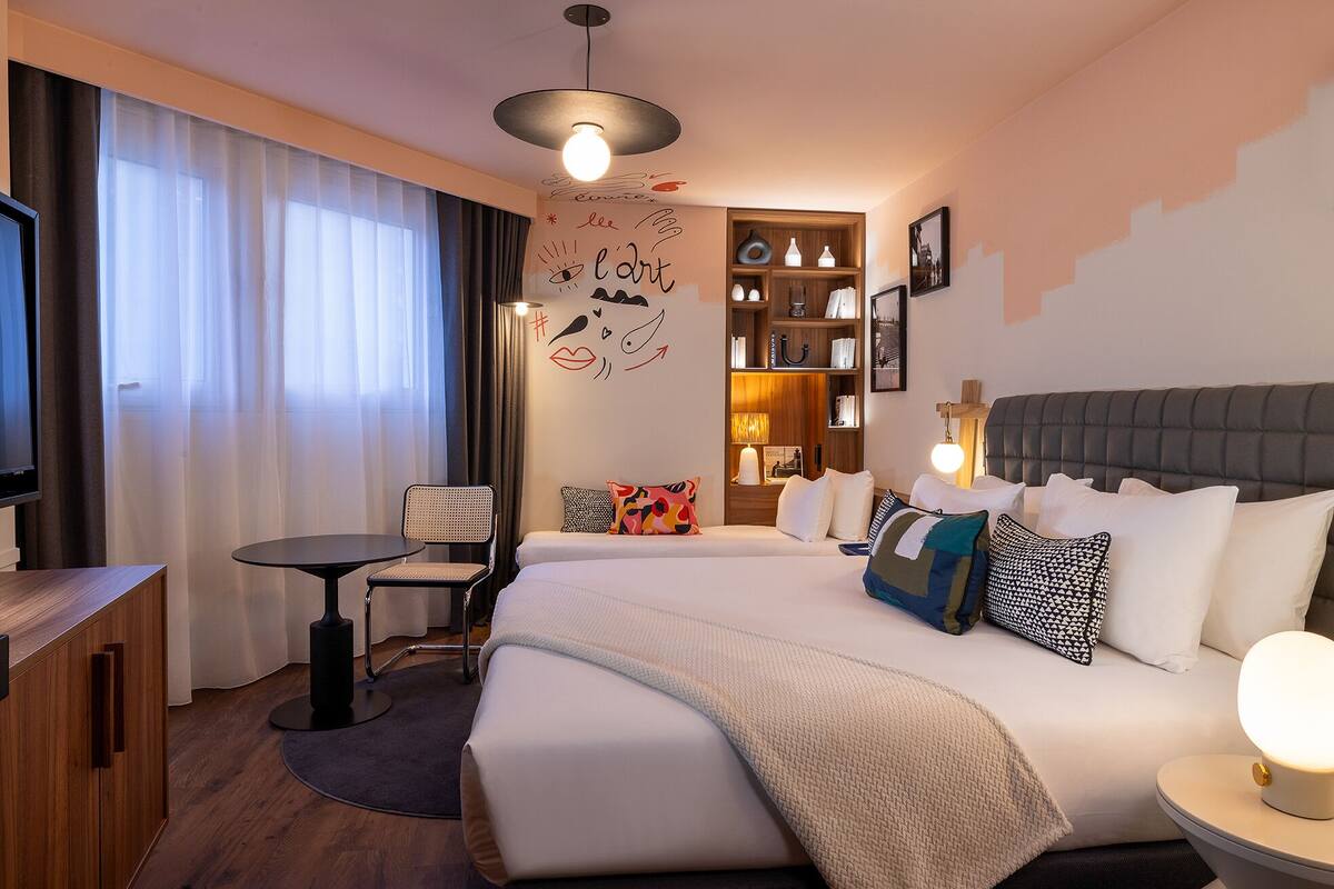 A hotel room with a bed, bedside table, chair, and a small desk with a TV.