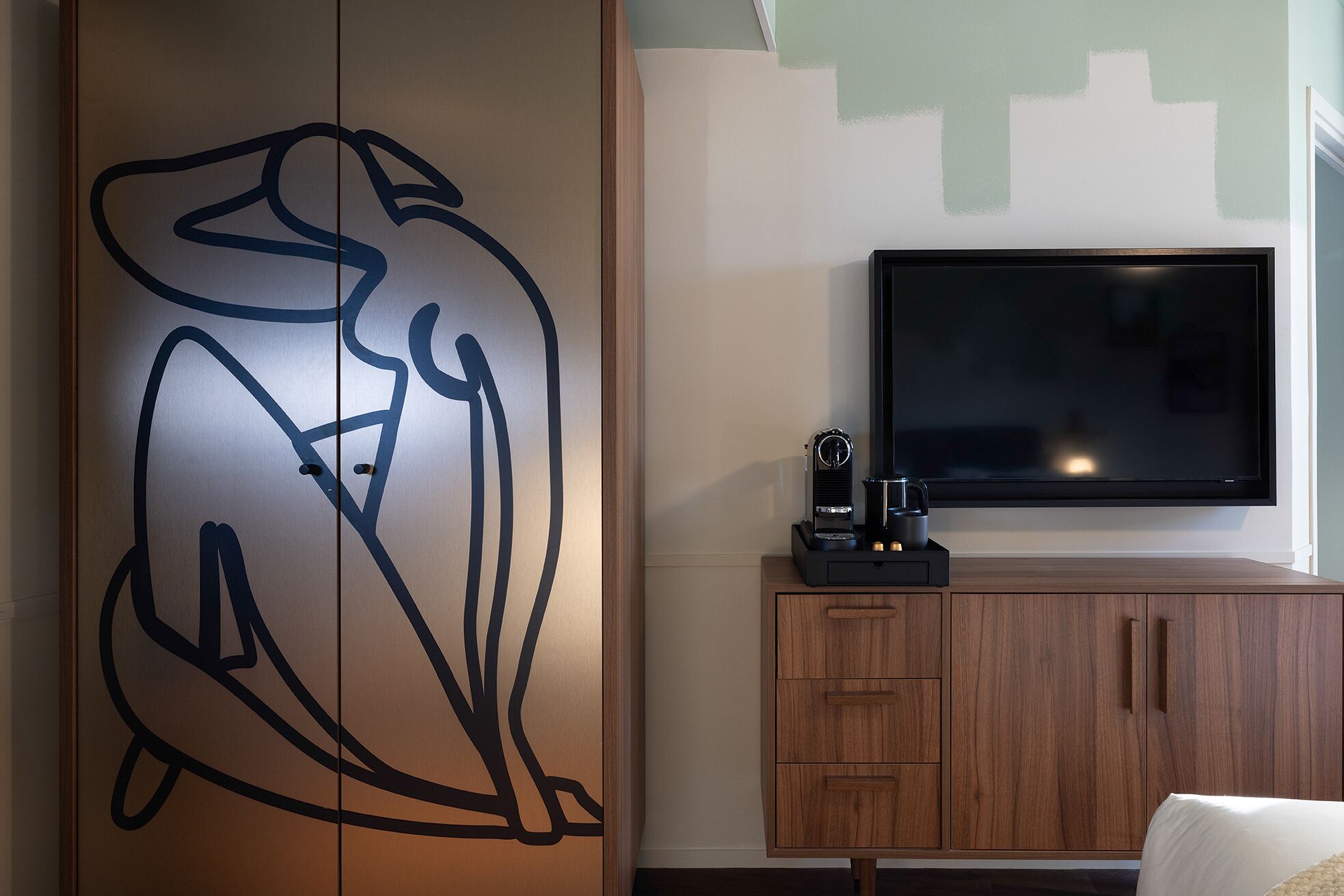 A room with a large abstract wall art, a flat-screen TV, a coffee machine, and a wooden cabinet.