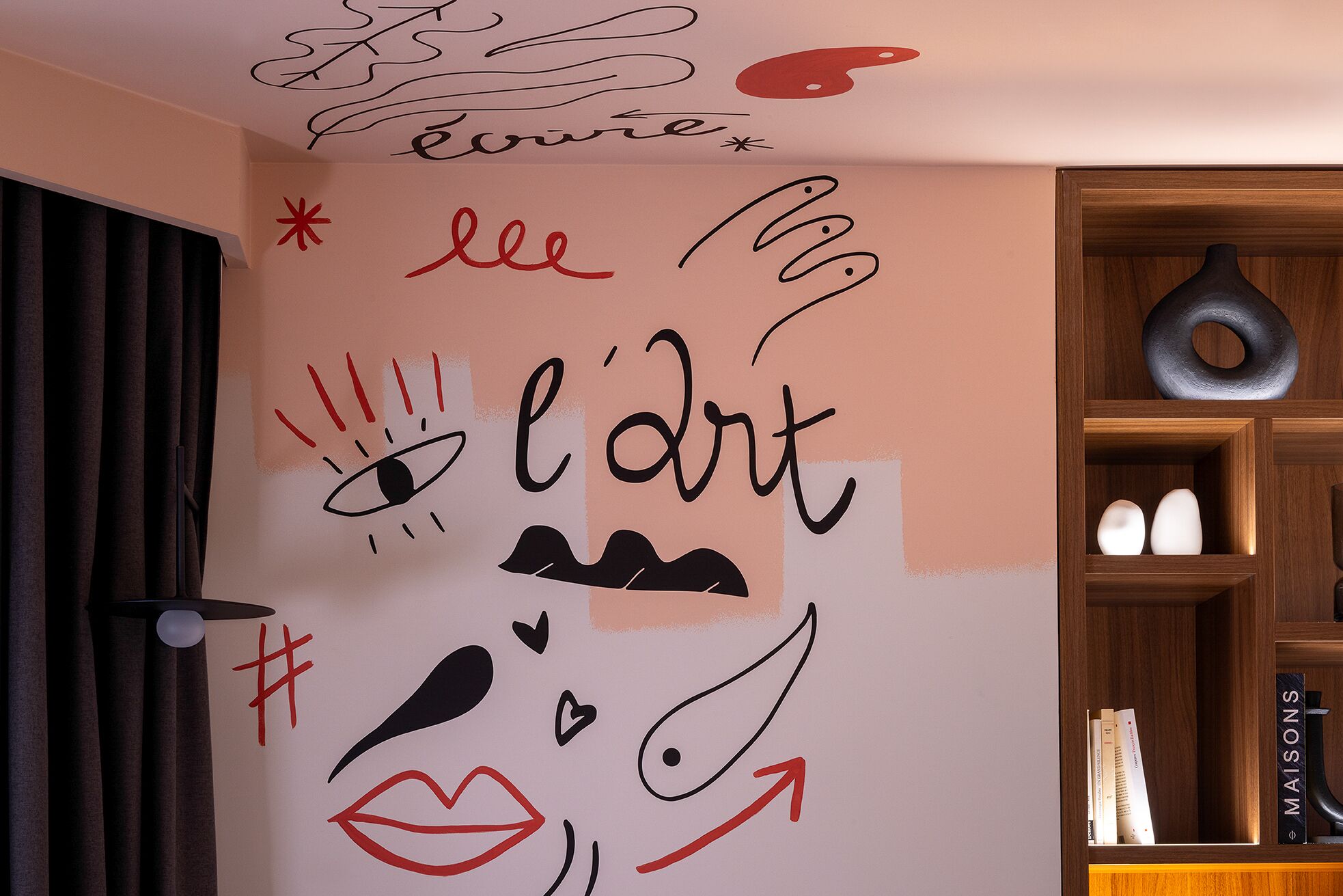 A wall with abstract art and text, a wooden shelf with books, and a door with curtains.