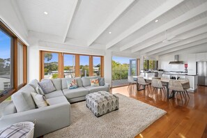 A modern open-plan living area with a sofa, ottoman, dining table, and chairs.