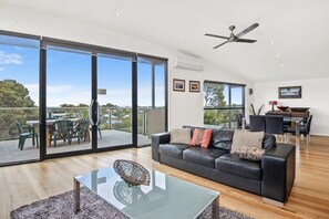 A modern living room with a glass coffee table, a black leather sofa, and a dining area with a glass table and chairs.