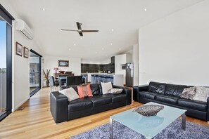 A modern living room with a black leather sofa, a glass coffee table, and a ceiling fan. - Seaview Sanctuary: Jan Juc Stay with Ocean Views (Jan Juc)
