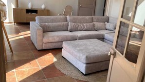 A living room with a sectional sofa, a wooden cabinet, a chair, and a door with a glass panel.