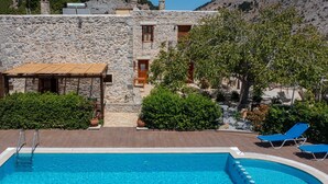 Edifici de pedra amb piscina, terrassa de fusta i gandules.