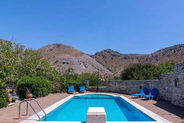 A swimming pool with blue chairs, a stone wall, and a mountainous backdrop. - Archodiko villa for 10 guests,Private pool,Near Sfakia (Chania)