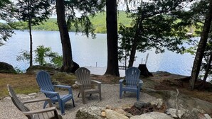 Uma área de estar à beira do lago, com cadeiras Adirondack e um espaço para fogueira.