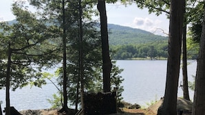Uma área de cascalho com uma lareira de pedra, rodeada por árvores e vista para um lago.