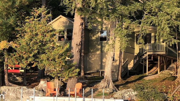 Uma cabana à beira do lago, com um píer, cercada por árvores e um deck de madeira.