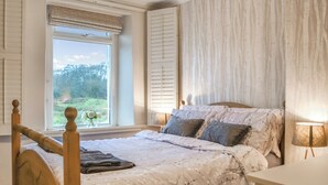 Een slaapkamer met een groot bed, een raam met uitzicht op groen, en een houten hoofdbord.