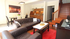 Una sala moderna con un sofá de cuero marrón, una zona de comedor con una mesa y sillas, y una cocina al fondo.
