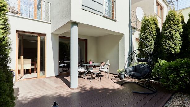 Un patio moderno al aire libre con una mesa de comedor y sillas, una silla colgante y un pequeño jardín con plantas en macetas.