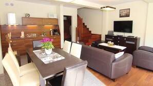 Una sala de estar moderna con una mesa de comedor, sofá y una cocina con armarios de madera y televisor.