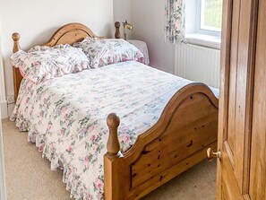 A wooden bed with floral bedding in a room with a window and a radiator.