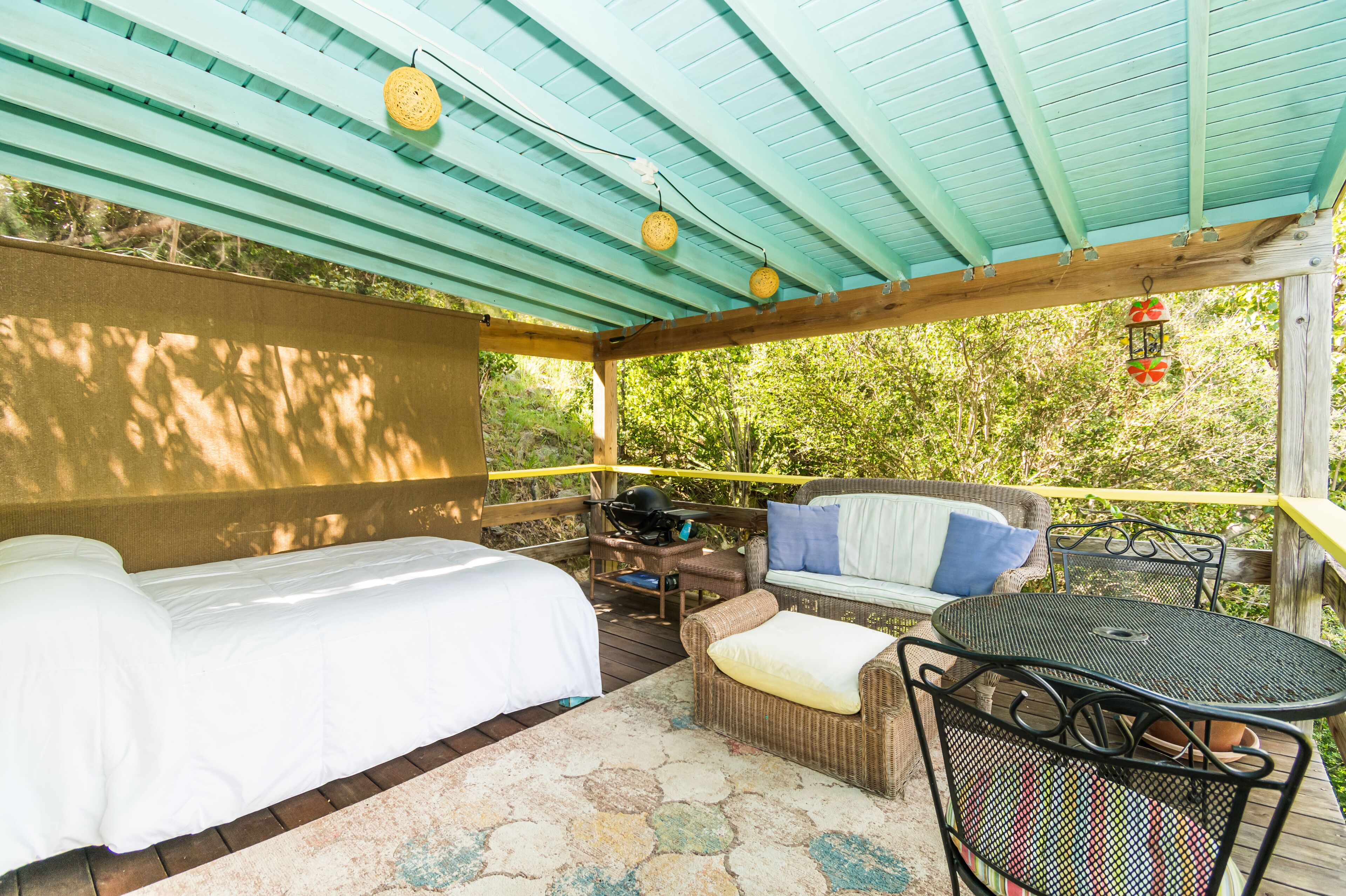 A covered outdoor seating area with two beds, a table, and chairs.