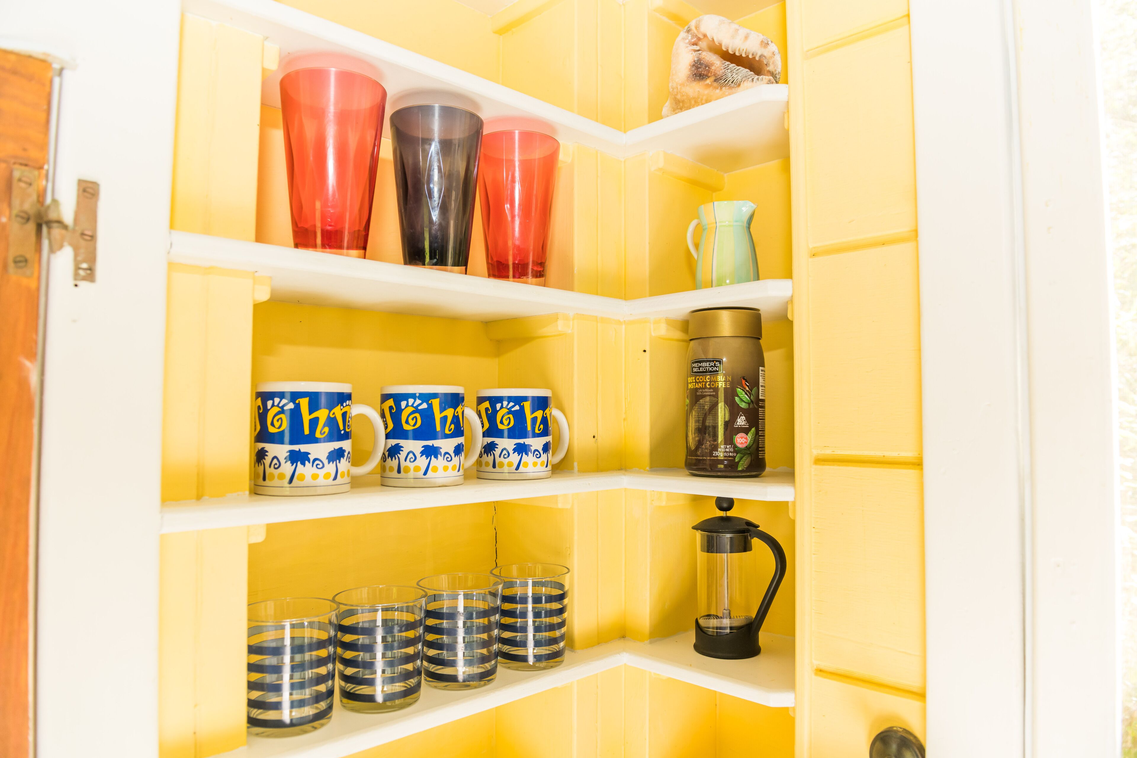 A yellow storage cabinet with shelves containing various items including mugs, a coffee maker, and glass containers.