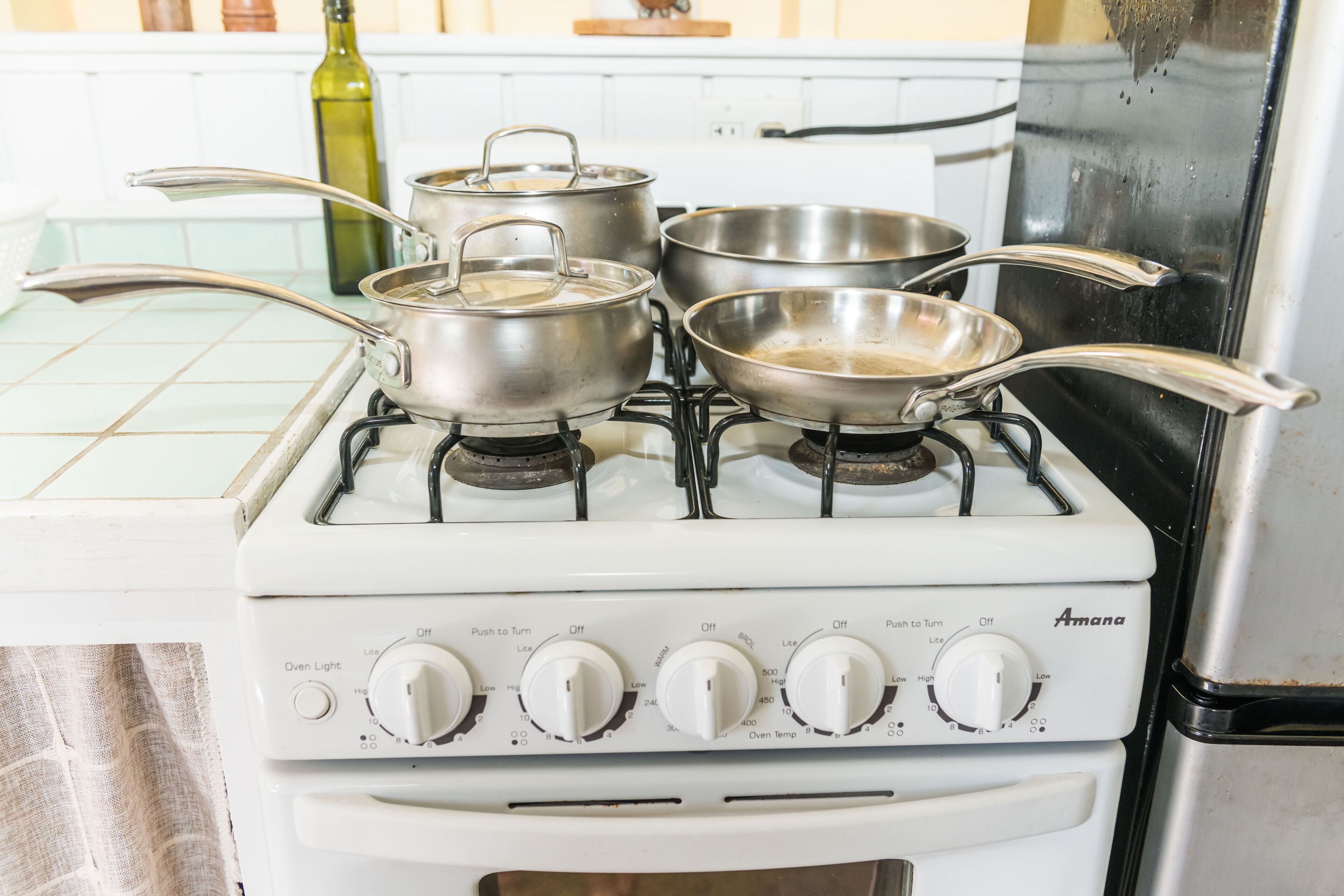 A kitchen with a white stove, pots, pans, and a bottle of olive oil.