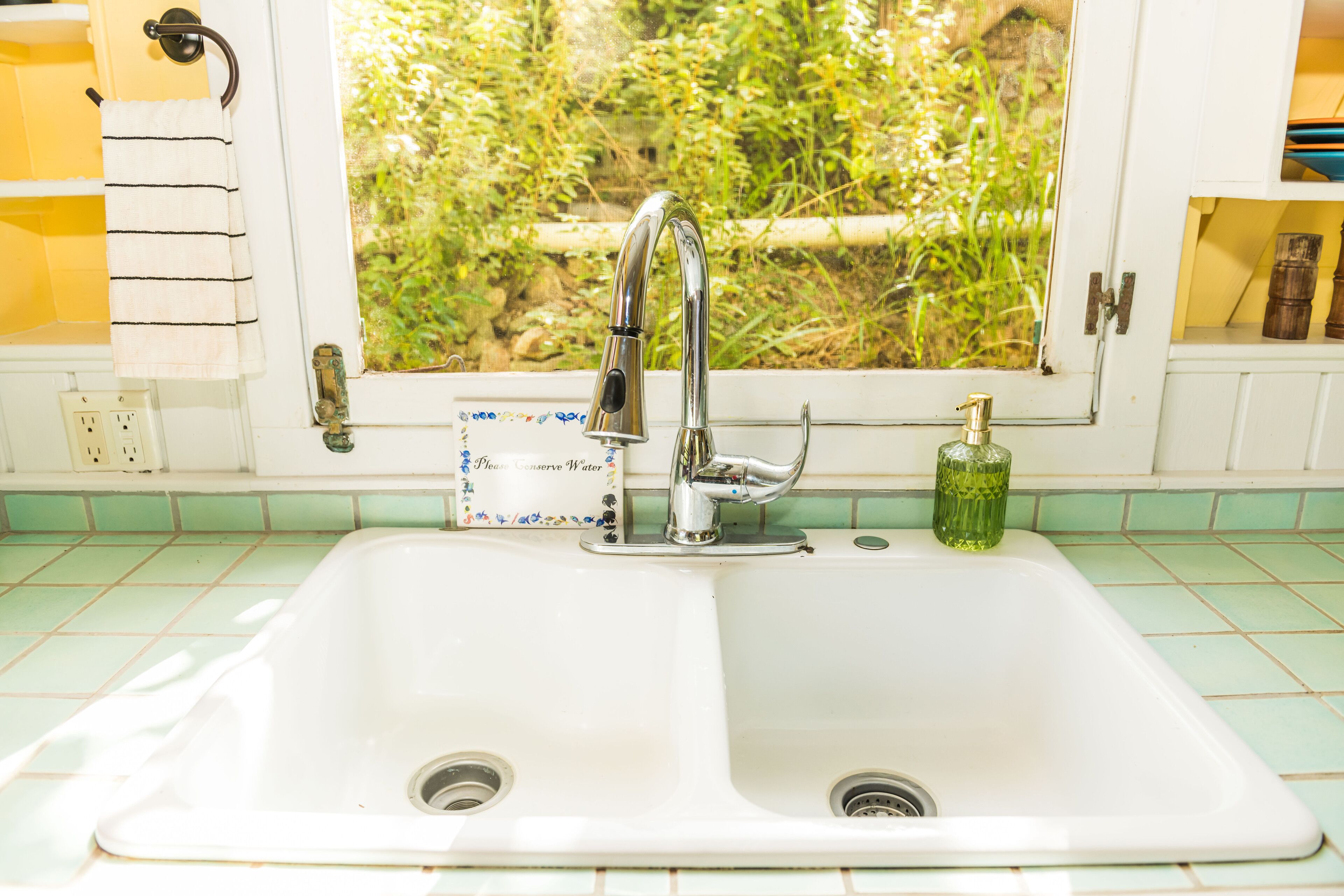 A kitchen sink with a window above it, a towel hanging on a rack, and a bottle of dish soap on the counter.