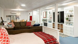 A cozy room with a brown sofa, a bed with red and white bedding, and a white built-in shelving unit with various items. - POOL, HOT TUB, PET FRIENDLY FENCED IN YARD RETREAT CLOSE TO LAKE MICHIGAN!!! (Coloma)