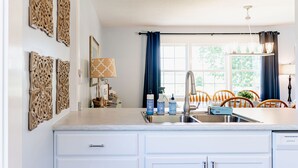 A modern kitchen with white cabinets, a stainless steel sink, and a window with blue curtains. - POOL, HOT TUB, PET FRIENDLY FENCED IN YARD RETREAT CLOSE TO LAKE MICHIGAN!!! (Coloma)