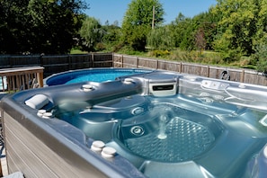 Relax in the hot tub with seating, surrounded by a deck with a fence and lush greenery.