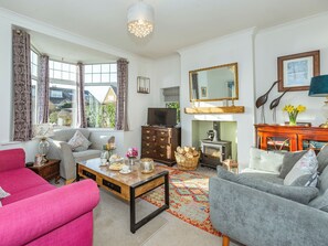 Un salon comprenant un canapé, un fauteuil, une table basse, une cheminée, un téléviseur et une vue sur l’extérieur.