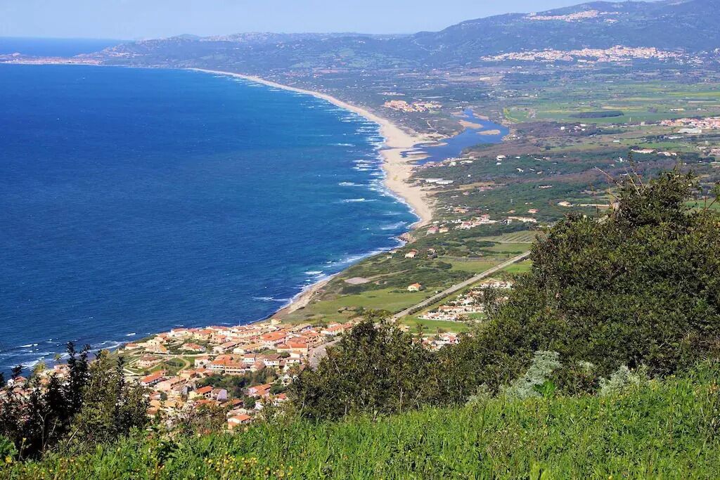 A coastal town with a beach, houses, and greenery.
