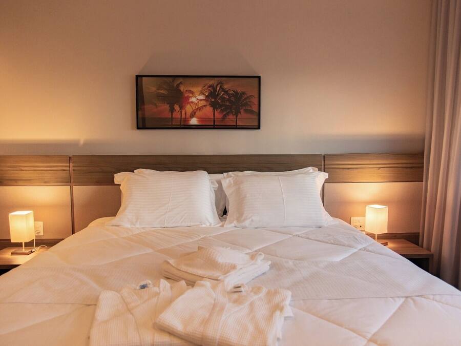 A neatly made bed with white linens and pillows, two bedside lamps, and a framed picture on the wall.