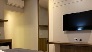 Una habitación de hotel con una cama grande, un televisor de pantalla plana montado en la pared y un equipo de aire acondicionado sobre la cama.