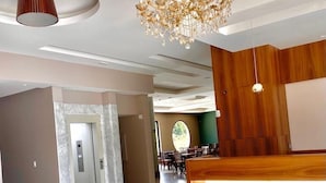 Un moderno vestíbulo de hotel con piso de mármol, mostrador de recepción de madera, una araña y vista al área de comedor.