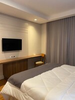 Habitación de hotel con cama, escritorio, silla, televisor y ventana con cortinas.
