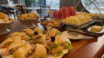 Een buffet met diverse etenswaren, waaronder sandwiches, croissants en watermeloen.
