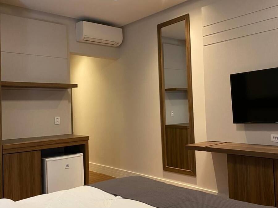 A modern hotel room with a bed, a TV, a mirror, and a small refrigerator.
