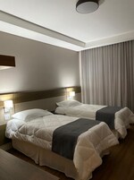 A hotel room with two beds, a wooden headboard, a large window with curtains, and a ceiling light fixture.