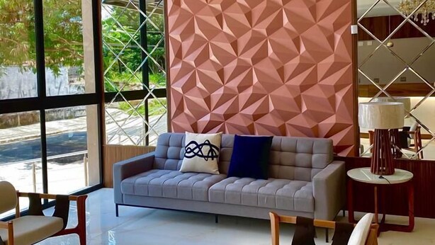 Una sala de estar moderna con un papel tapiz de diseño geométrico, un sofá gris, sillas de madera y una mesa de centro de vidrio.