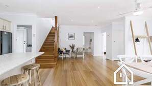 Un vaste espace de vie agrémenté d’un escalier en bois, une cuisine dotée d’un plan de travail en marbre et un coin repas avec des chaises blanches.