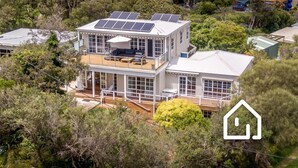 Une maison à deux étages dotée d’un balcon, de panneaux solaires et d’une grande terrasse.