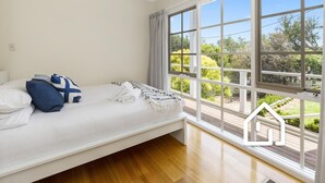 Une chambre à coucher avec un lit, des oreillers, une couverture et une grande fenêtre donnant sur un paysage verdoyant.