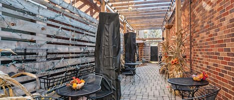 Un patio cubierto con paredes de ladrillo, vigas de madera y mesas y sillas de metal.