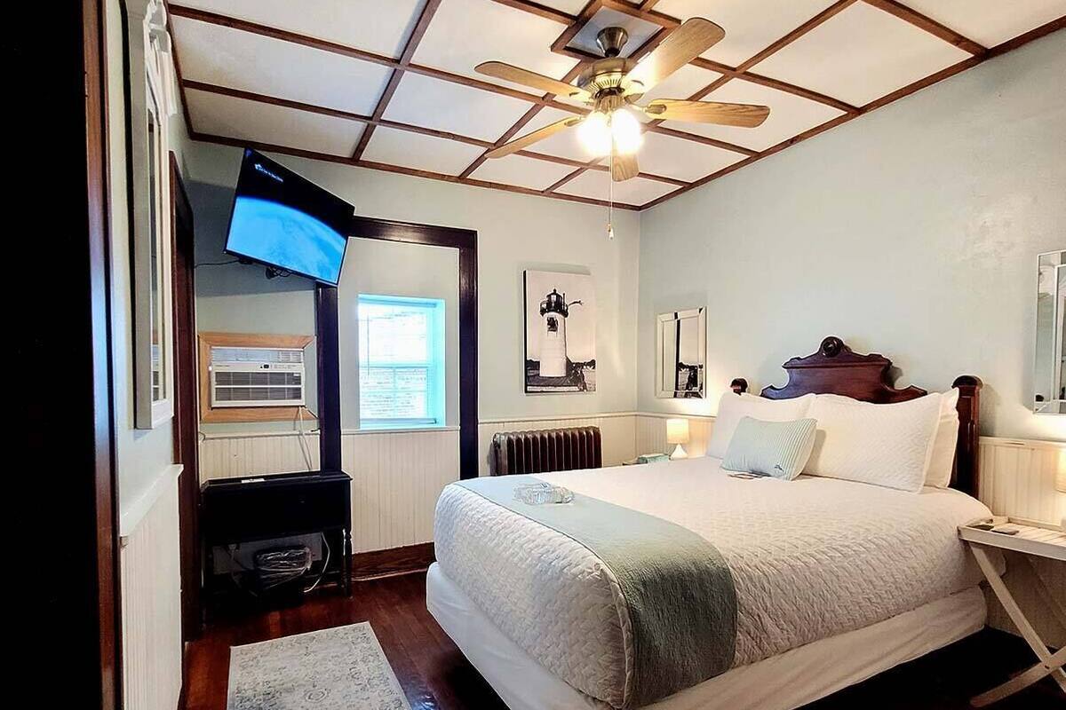 Un dormitorio con una cama, ventilador de techo, televisión y ventana.