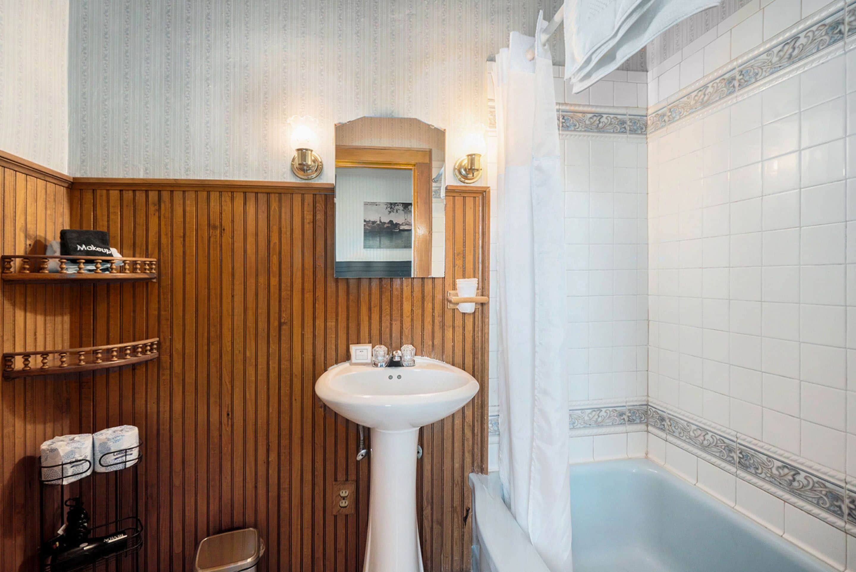 Un baño con paneles de madera, un lavabo blanco, un espejo y una bañera.