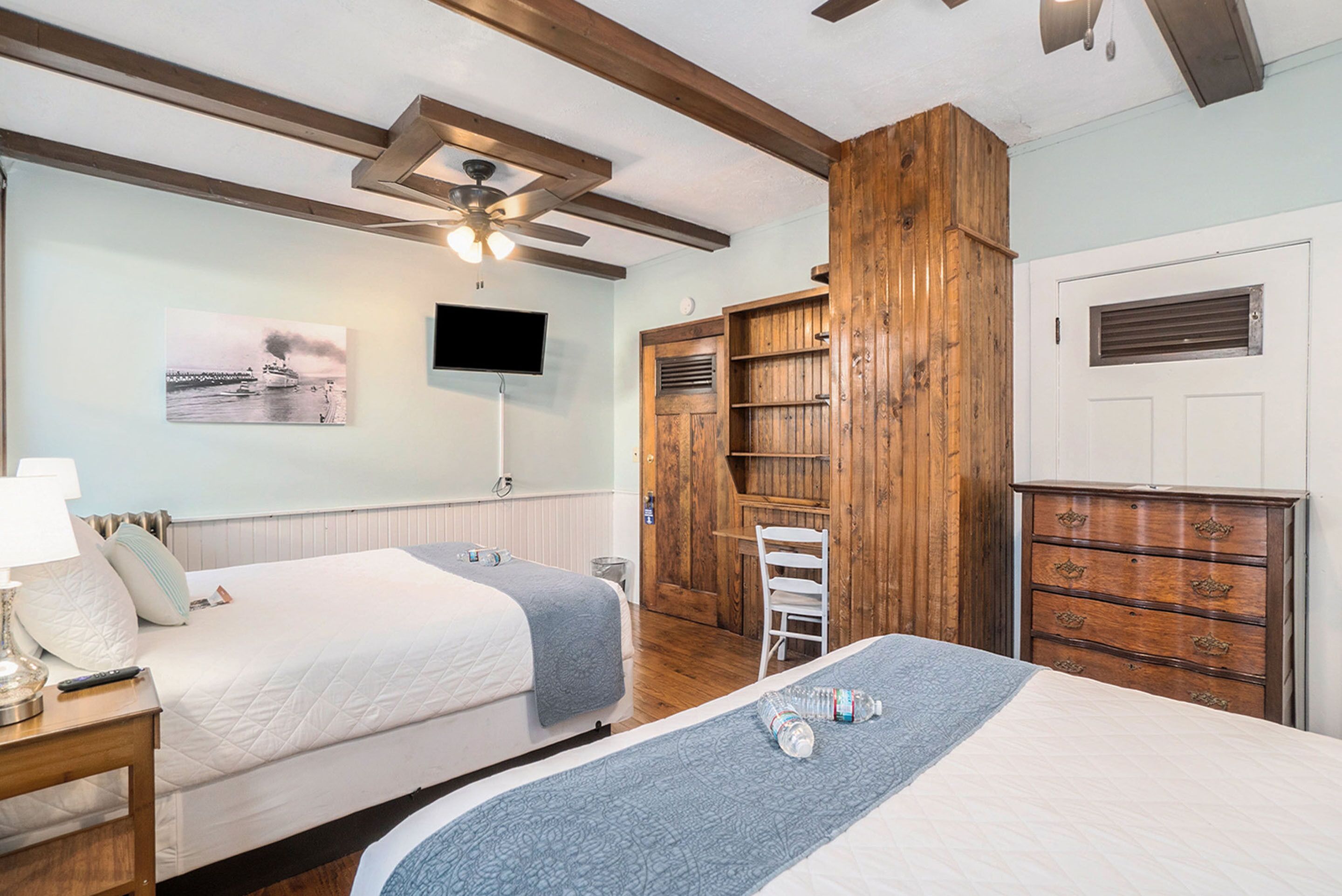 Habitación de hotel con dos camas, un escritorio, una silla, un televisor y un armario de madera.