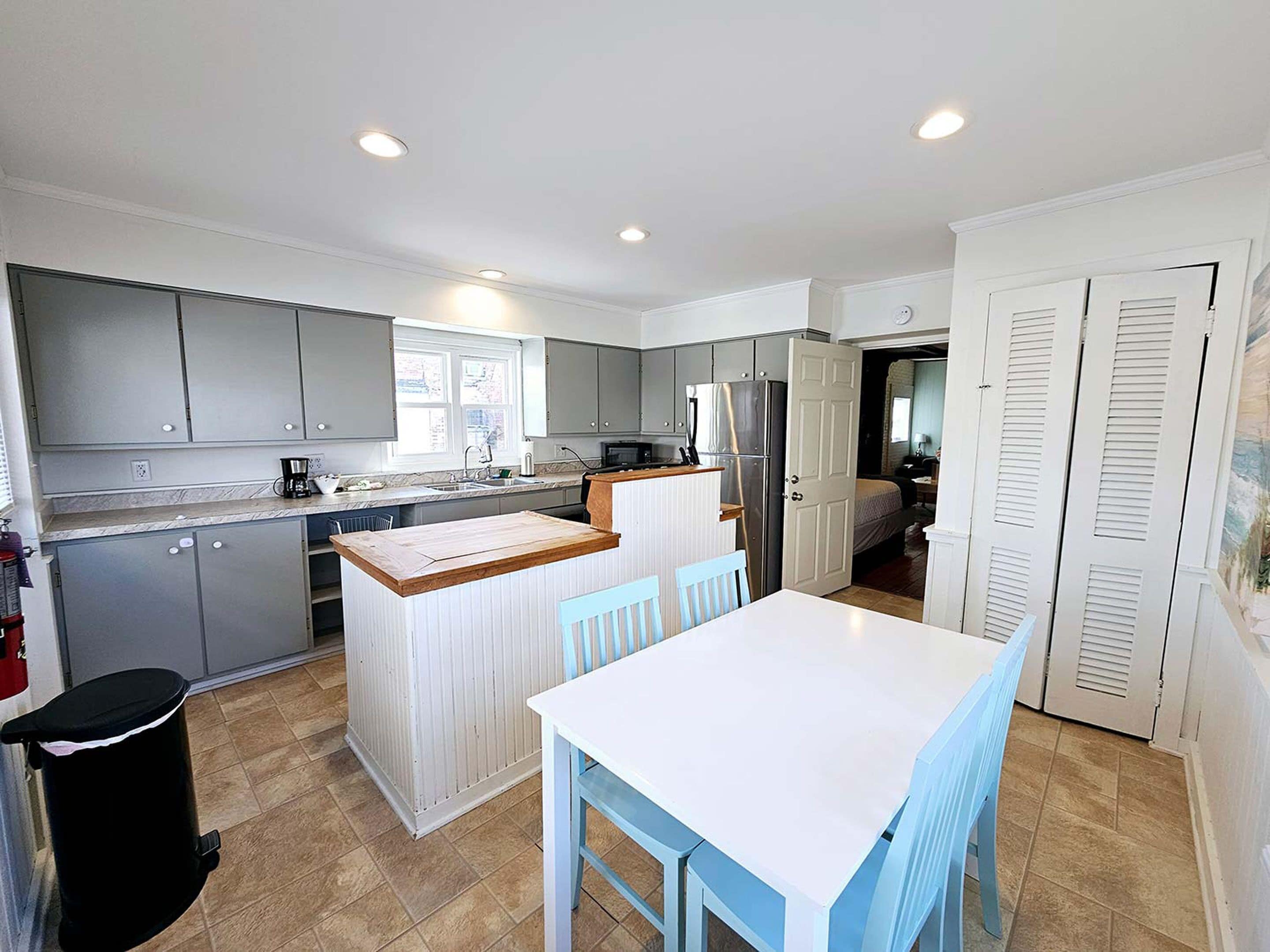 A compact kitchen with grey cabinets, a white island, and a dining area with blue chairs.