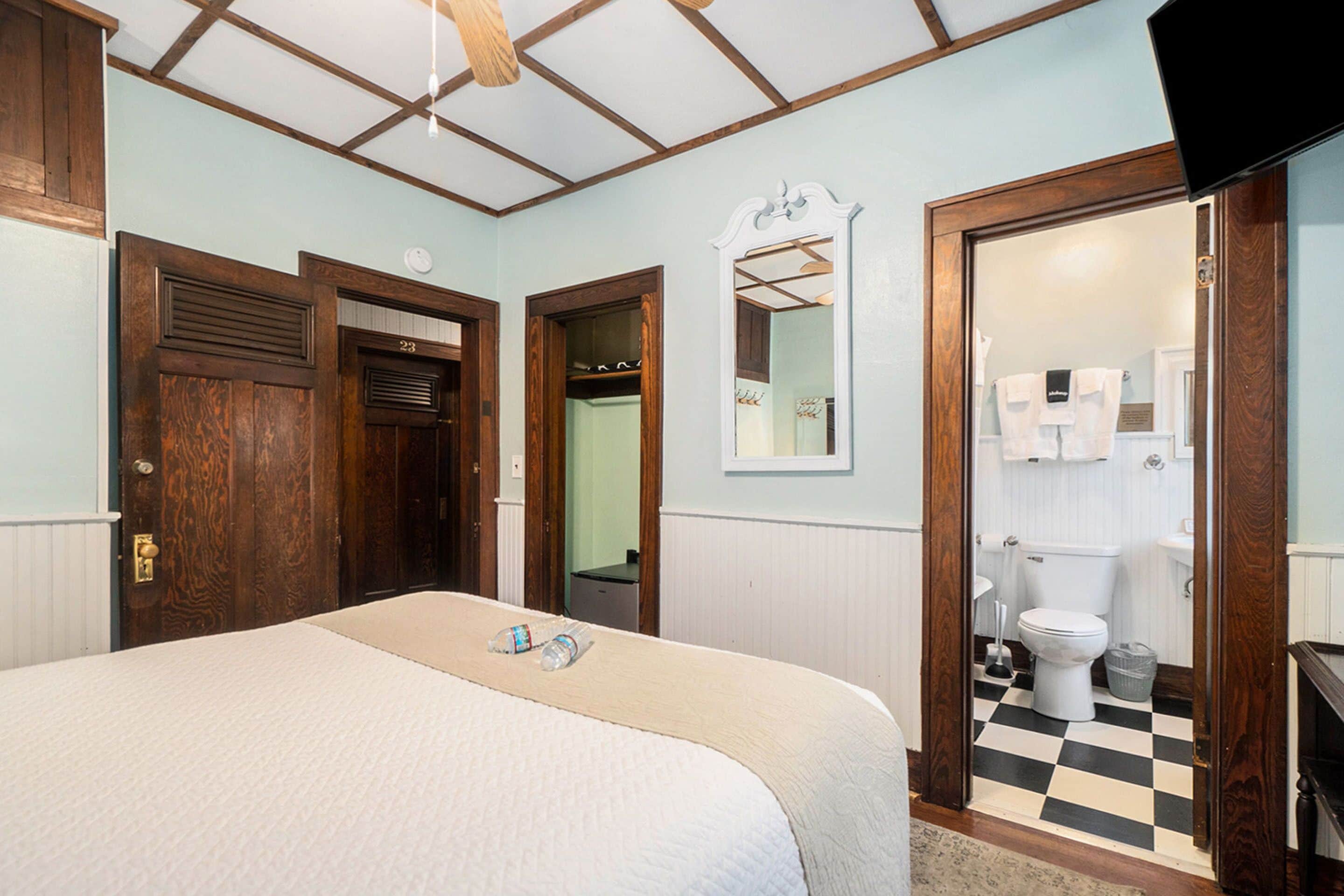 A bedroom with a bed, wooden doors, a mirror, and a view into the bathroom.