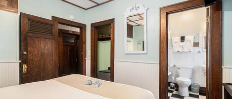 A bedroom with a bed, wooden doors, a mirror, and a view into the bathroom.