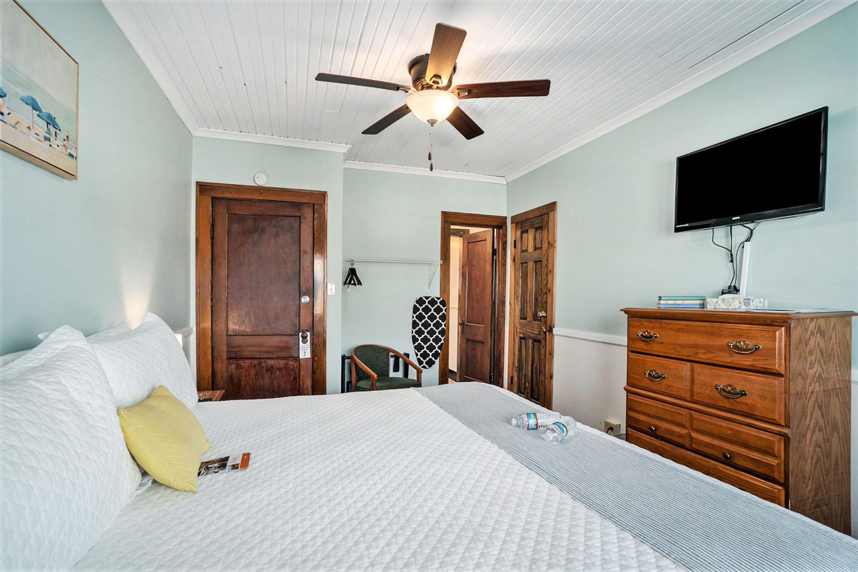 Une chambre à coucher comprenant un lit, une commode, un téléviseur et un ventilateur de plafond.