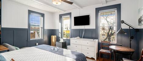 A bedroom with a bed, dresser, chair, desk, and TV.