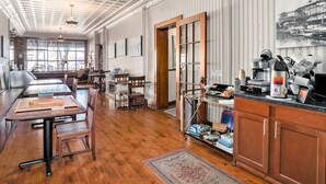 Um quarto amplo com piso de madeira, uma grande mesa de jantar e uma cozinha equipada com cafeteira e utensílios.
