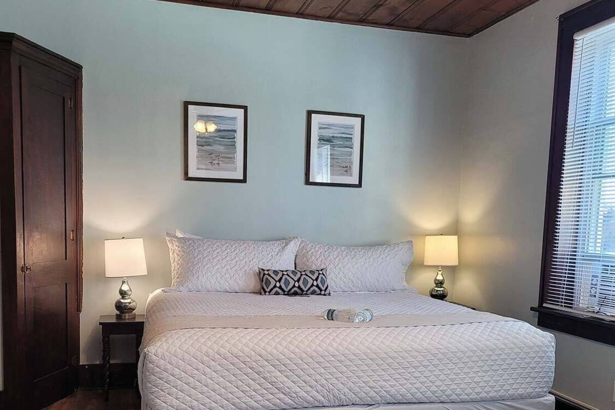 Un dormitorio con una cama grande, dos lámparas de noche, techo de madera y dos cuadros en la pared.