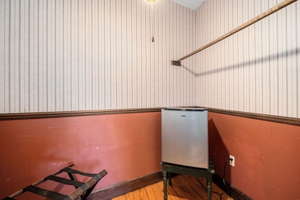 A corner room with a white-striped wall, a red lower section, and a small refrigerator on a stand. - Historic Hotel Nichols (South Haven)